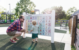 Child using a low-tech playground communication board featuring AAC picture symbols